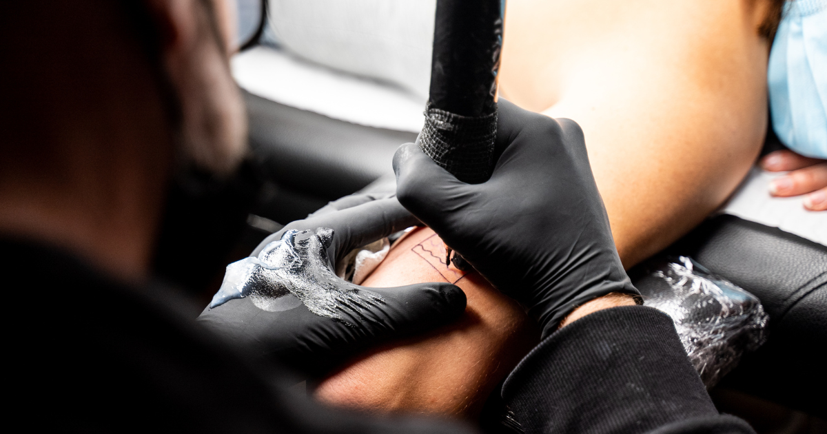 Tatuador con guantes de nitrilo negros realizando un tatuaje